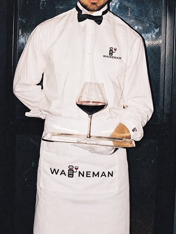 Een ober met WAINEMAN-schort draagt een glas rode wijn op een dienblad